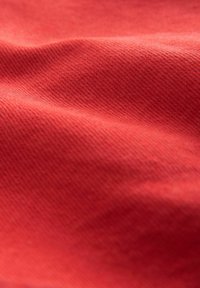 Tissu rouge avec une texture tissée visible et des plis doux créant des ombres subtiles et des reflets sur toute la surface.