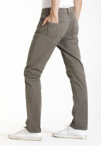 Pantalons stretch gris clair pour hommes avec cinq poches, coupe slim et texture douce, associés à des baskets blanches.