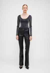 Langärmliges, figurbetontes Oberteil aus glitzerndem Schwarz und Silber; kombiniert mit hochgeschnittenen, glänzenden, schwarzen Kunstlederhosen und spitzen Schuhen.