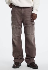 Grijze cargobroek met een losse pasvorm, voorzien van meerdere zijzakken en een vervaagde textuur. Gemaakt van duurzaam stof met zichtbare stiksels.