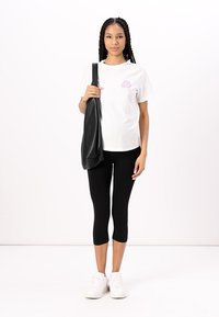 Svart skinn skulderveske, hvit t-skjorte med korte ermer og rosa grafikk, svarte capri leggings og hvite joggesko. Enkle hverdags klær.