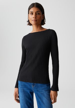 Schwarzes, geripptes Langarmoberteil mit Bootsausschnitt, aus einem weichen Material gefertigt. Kombiniert mit blauen Jeans, die eine figurschmeichelnde Silhouette zeigen.