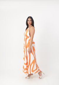 Maxi kjole i hvid med orange abstrakte mønstre; halterneck, elastisk talje, let stof, parret med hvide hæle med struktureret design.