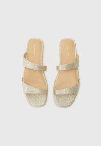 Gold glitter slide sandals with two crisscross straps, square toe, flat sole, and a neutral beige footbed with subtle branding.