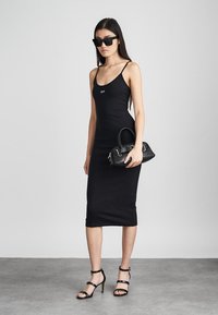 Rochie midi neagră, ajustată, cu bretele subțiri și un logo vizibil. Asortată cu o poșetă mică neagră și sandale cu toc subțire negre.