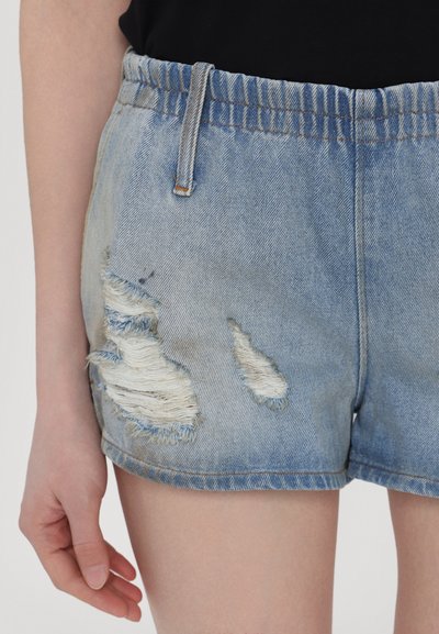 Svetlomodré denim šortky s roztrhnutým okrajom, ktoré obsahujú viaceré postrhnuté škvrny a elastický pás.