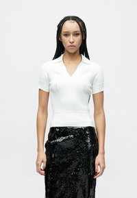 Top de malha canelada branca com decote em V e mangas curtas, combinado com uma saia lápis preta com lantejoulas. Textura suave, design justo.