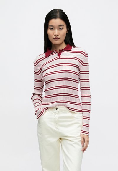 Polo à manches longues rayé rose et rouge, avec une texture côtelée, un col rouge et une coupe slim, associé à un pantalon blanc.