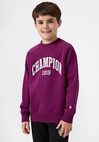Felpa viola realizzata in tessuto morbido con la scritta "CHAMPION" e "1919" in caratteri bianchi. Ha un collo rotondo e polsini a costine.