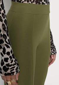 Leggings verdes-oliva de cintura alta feitos de um tecido macio apresentam uma textura suave e costuras mínimas, combinados com uma blusa com padrão de leopardo em preto e branco.