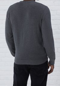 Pull en tricot gris à manches longues, col rond et ourlet côtelé ; sans motifs ni éléments métalliques visibles. Vue de dos avec une texture lisse.