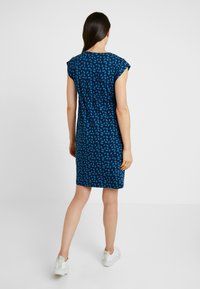 Krótkosleeve, sukienka do kolan w kolorze granatowym z geometrycznym wzorem w kolorze zielonego turkusu. Ma okrągły dekolt i dopasowaną talię.