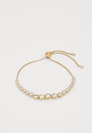 Arany színű, állítható karkötő, átlátszó, kerek strasszokkal, sima felülettel és csúszó golyós zárómechanizmussal.