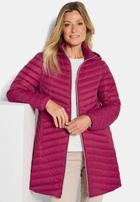 Fuchsiakleurige pufferjas met een ritssluiting aan de voorkant, capuchon en gestepte ontwerp. Voorzien van zijzakken en een iets langere achterzoom voor extra bedekking.