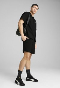 Czarna koszulka krótki rękaw o fakturowanym wykończeniu, czarne szorty, czarne sneakersy Puma z białymi akcentami oraz mała czarna torba na ramię.