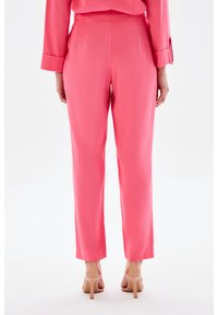 Pantalon rose sur mesure avec une texture lisse et une coupe droite. Il présente une taille mi-haute et une longueur raccourcie au-dessus de la cheville.