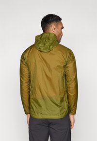 Green lightweight jacket with a matte finish, adjustable hood, and seams; designed for comfort and mobility, showcasing a sleek silhouette.
