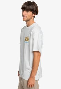 White cotton t-shirt with short sleeves. Features a gold and blue graphic design on the chest. Relaxed fit and soft texture.