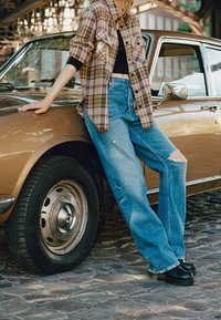 Rutig flanellskjorta i brunt och lila, svart crop top, slitna ljusblå jeans och svarta platåskor bredvid en vintagebil.