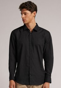Zwarte langemouwen shirt van lichtgewicht stof, met een knoopsluiting aan de voorkant, een puntige kraag en een ontspannen pasvorm.