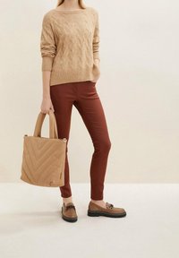 Beige svetr s pleteným vzorem, hnědé slim fit kalhoty, hnědé mokasíny s řetízkovým detailem a béžová taška s chevron vzorem.