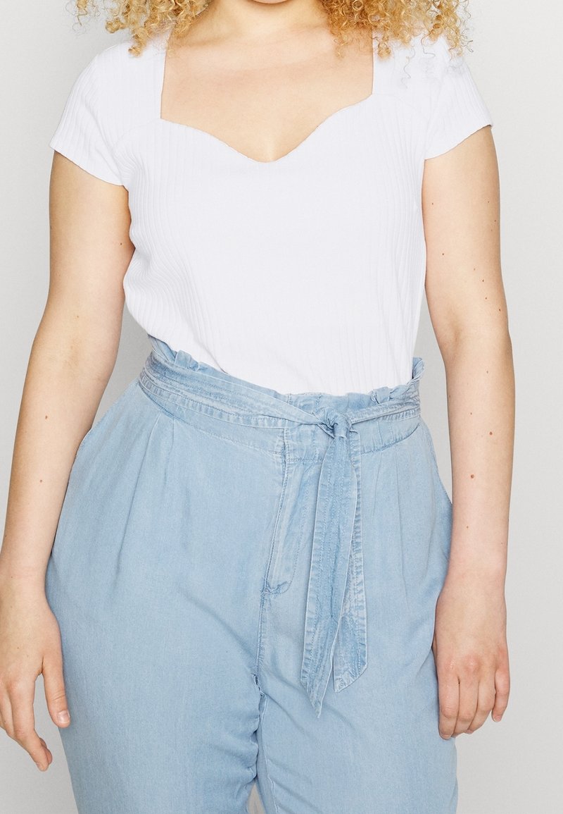 Vit ribbad topp med fyrkantig halsringning, i kombination med ljusblå högmidjade byxor med knytbälte och avslappnad passform.