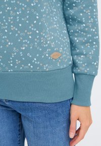 Felpa blu con motivo maculato in azzurro chiaro e beige, polsini e orlo a coste, con una piccola targhetta logo color sabbia.