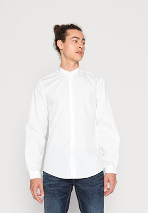 Camicia bianca con colletto eretto, maniche lunghe e chiusura frontale con bottoni. Il tessuto appare liscio e leggermente lucido.