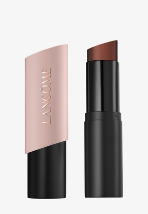 Fond de teint stick marron foncé avec base noire et capuchon arrondi rose-beige embossé du nom "Lancôme" à côté sur fond blanc.
