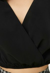 Top cropped nero con scollatura a V profonda, realizzato in tessuto liscio. Presenta un orlo arricciato e un design avvolgente, che enfatizza una silhouette aderente.