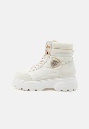 Botte d'hiver blanche montante avec semelle épaisse, œillets dorés, détail matelassé sur le côté et doublure en fausse fourrure visible au col.