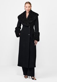 Czarny płaszcz z dużym, teksturowanym kołnierzem i mankietami, o prostym kroju, z zapięciem na guziki oraz luksusowym wykończeniem tkaniny.