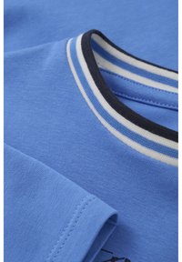 Camisa de manga corta azul claro con un cuello acanalado con franjas en azul marino y blanco. Tejido liso de un solo color sin patrones visibles.