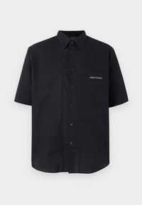 Chemise noire à manches courtes avec col et logo Armani Exchange sur la poche poitrine gauche, présentée sur un fond clair.