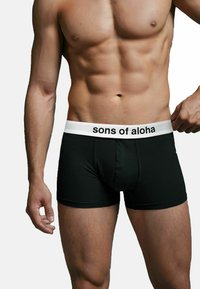Boxer briefs neri in cotone con una fascia bianca con il testo "sons of aloha", che mostrano una vestibilità aderente e una texture liscia.
