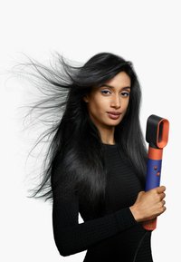 Asciugacapelli dal design elegante, con un ugello arancione e un corpo blu, tenuto da una persona con lunghi capelli neri lisci.