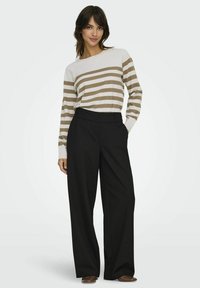 Pull rayé en crème et beige, associé à un pantalon noir à jambes larges. Le pull a des manches longues et un col rond, avec une texture lisse.