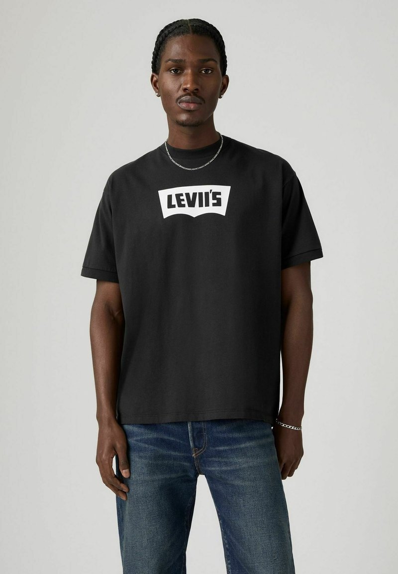 T-shirt en coton noir avec un logo Levi's blanc sur le devant. Manches courtes et coupe décontractée. Porté avec un jean bleu.