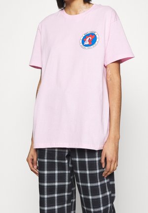 T-shirt en coton rose clair avec un patch graphique rond au design rouge et bleu. Coupe décontractée avec manches courtes, col rond et ourlet droit.