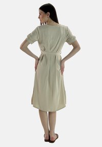 Abito beige fino al ginocchio realizzato in tessuto morbido. Presenta maniche corte arrotolate, una vita con cintura e una gonna leggermente svasata.