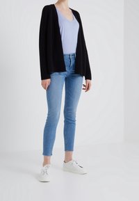 Svart stickad cardigan, ljusblå v-ringad topp, ljusblå skinny jeans och vita sneakers. Cardiganen har en öppen framtill-design och ribbat mönster.