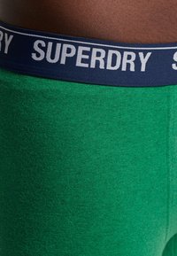 Groene katoenmix boxershorts met een marineblauwe elastische tailleband waarop het "SUPERDRY"-logo in het wit is gedrukt. Zachte textuur, aangesloten ontwerp.