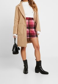 Beige wool coat with large pocket, white ribbed sweater, pink plaid mini skirt, and black heeled ankle boots. Black handbag with textured finish.