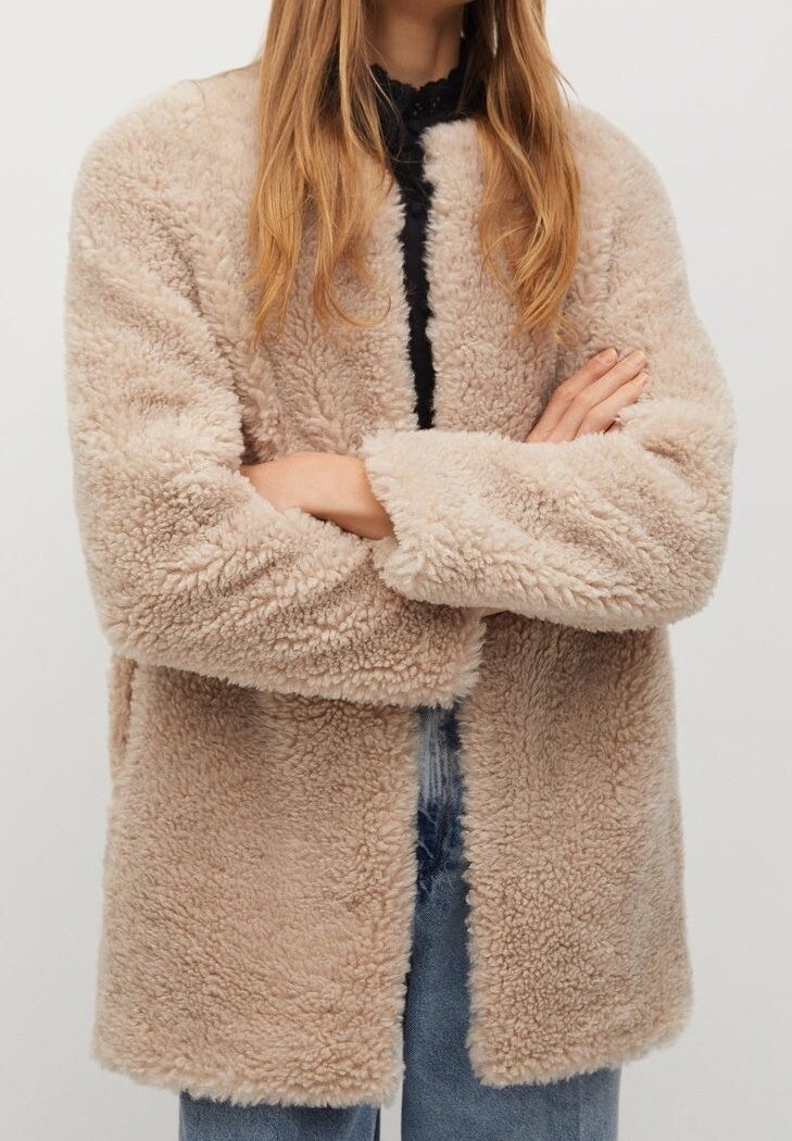 Lys beige falsk pelsjakke med en blød, tekstureret overflade, åben front og brede ærmer. Har en afslappet pasform og minimalistisk design.