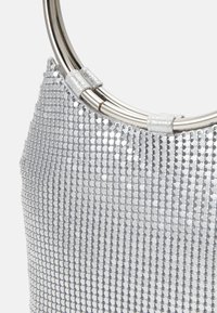 Sac à main en filet argenté avec des poignées métalliques circulaires et une surface texturée et brillante.