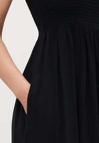 Μαύρο φόρεμα με τσέπες στο πλάι, διαθέτει φάσες στο μπούστο και ρέουσα φούστα. Το ύφασμα φαίνεται μαλακό με ματ υφή.