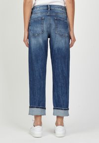 Mörkblå, något urtvättad denimjeans med avslappnad passform, uppvikta fållar och två bakfickor. Bärs med vita sneakers.