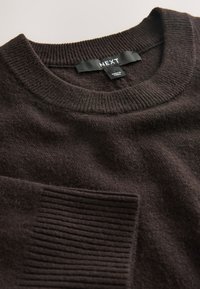 Pull en maille marron foncé avec col rond côtelé et poignets, avec étiquette de vêtement "NEXT".