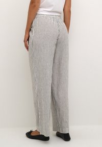 Striped wide-leg trousers in lightweight fabric, featuring black and white vertical stripes, elastic waistband, and side slits at the hem.