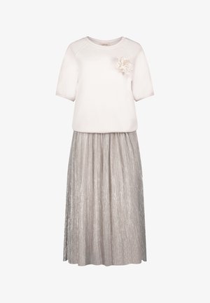 Witte top met korte mouwen, voorzien van een stofbloemaccent, gecombineerd met een zilveren geplooide rok. De stof heeft een glanzende textuur.